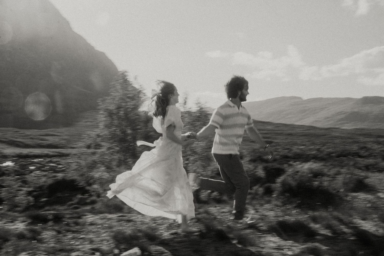 A couple running playfully through a mountainous landscape during their wedding shoot.