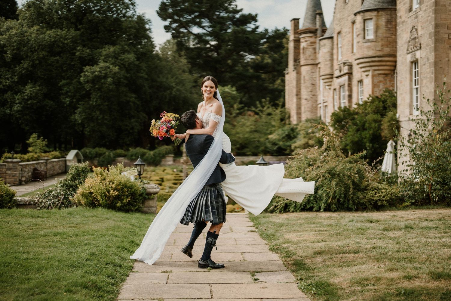 A couple shares a romantic moment outside a historic stone castle building during their wedding celebration.
