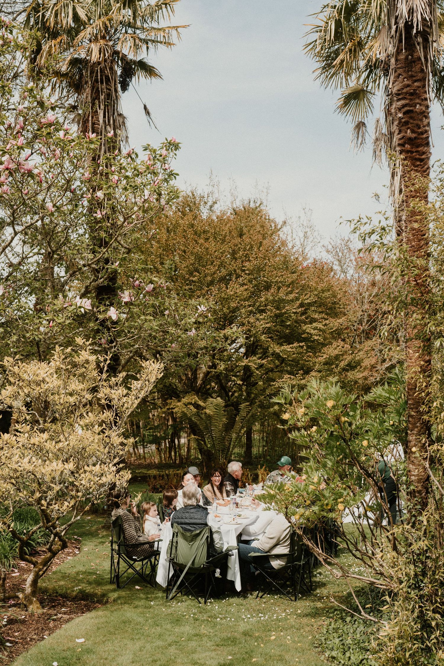 Outdoor garden party setup with white tablecloth under palm trees.