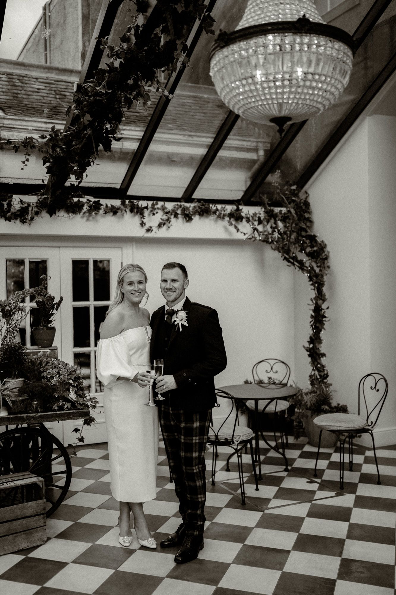 Wedding couple dancing on a black and white checkered floor under crystal chandeliers.