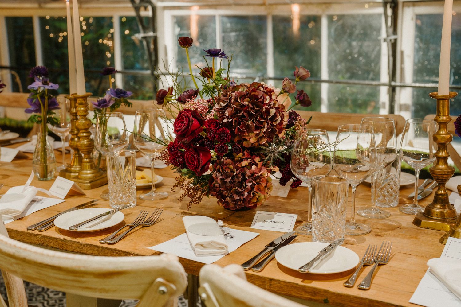 Elegant table setting with deep red floral centerpiece and crystal glassware for wedding reception.
