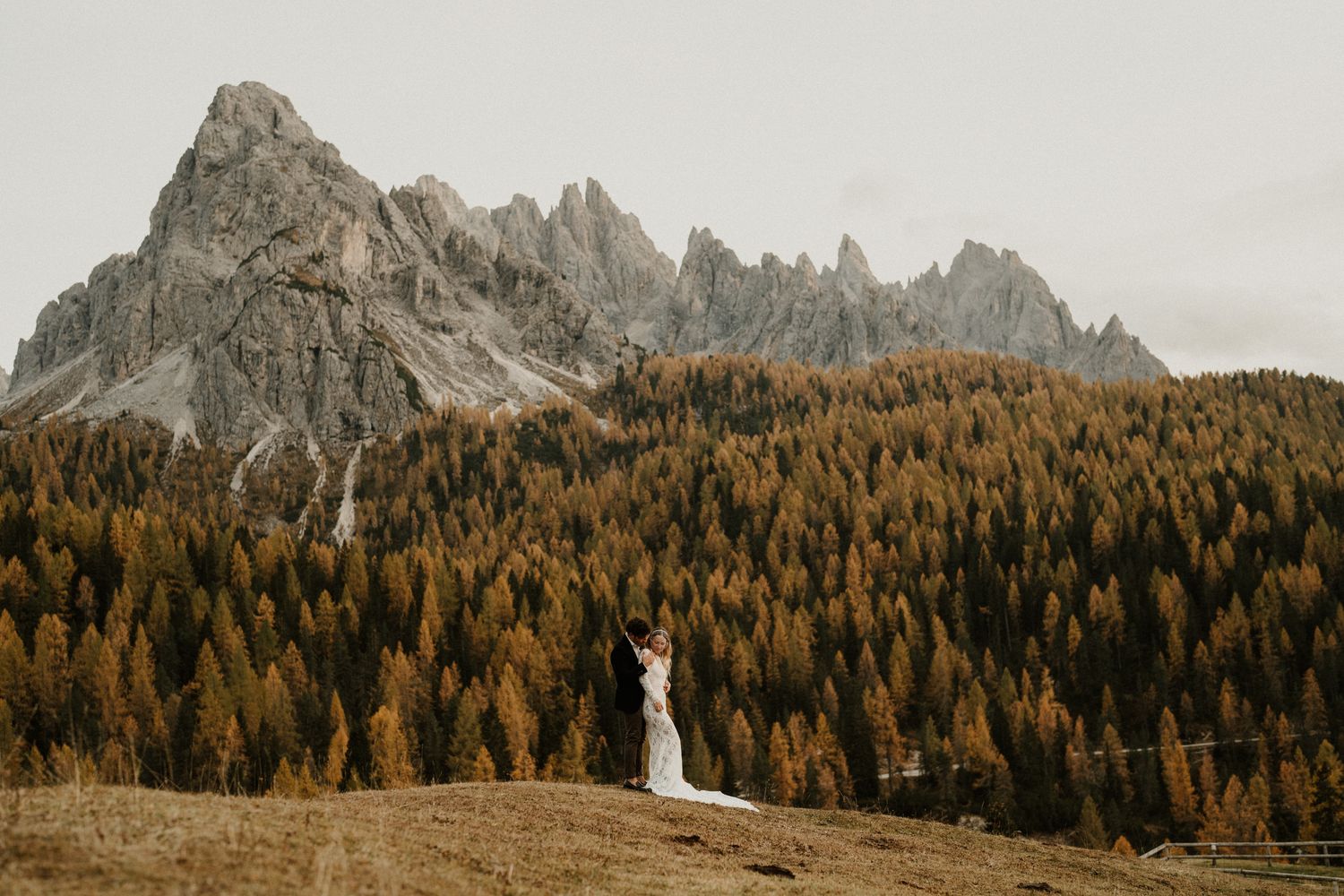 Distant view of wedding couple against majestic mountain peaks and golden forest.