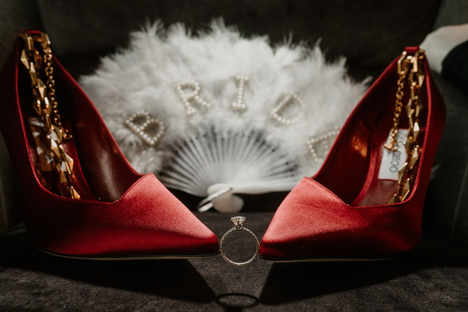 Wedding accessories including red shoes and delicate white fan arranged on dark background.