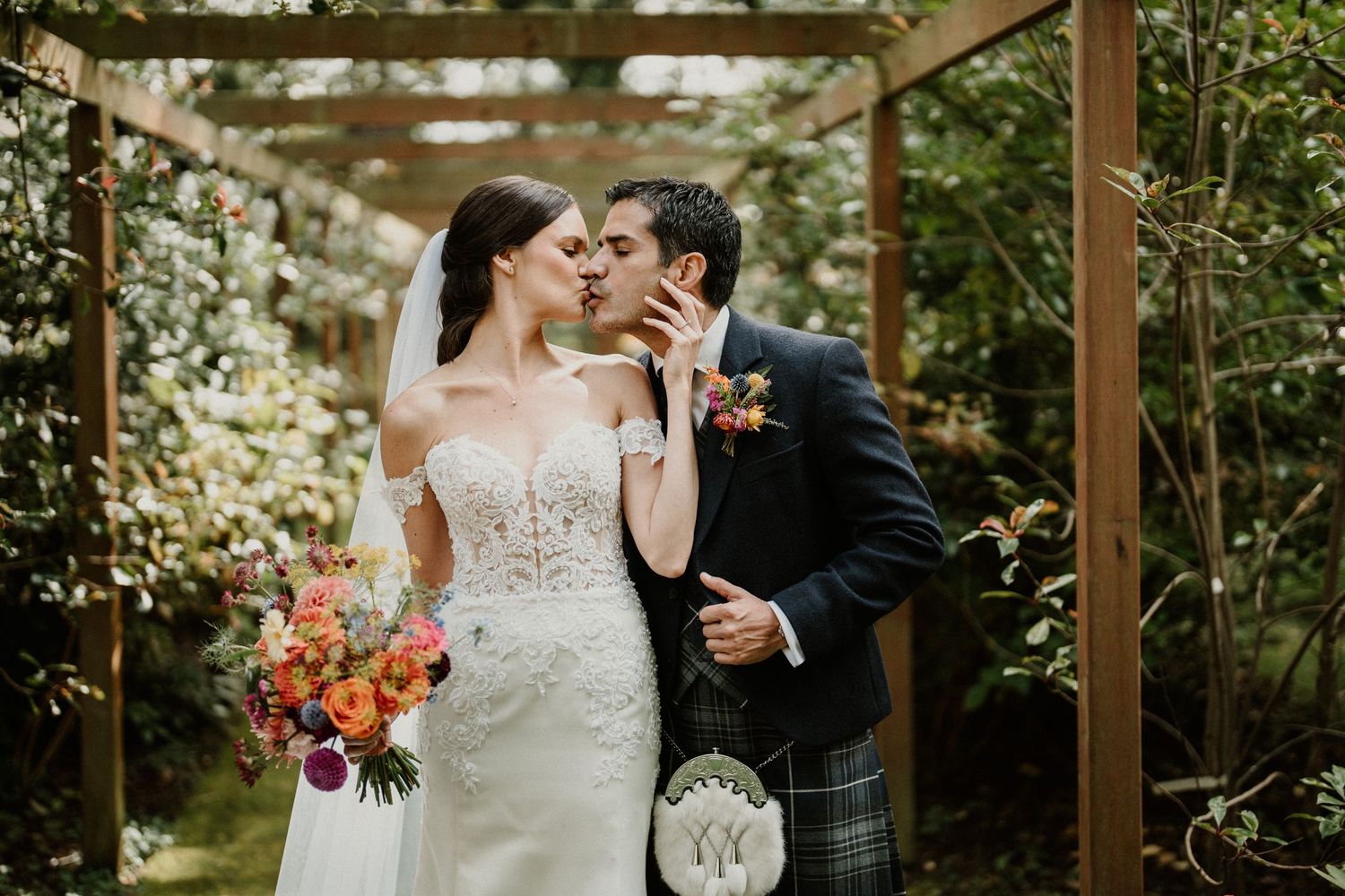 Intimate wedding ceremony moment under a wooden pergola decorated with floral arrangements.