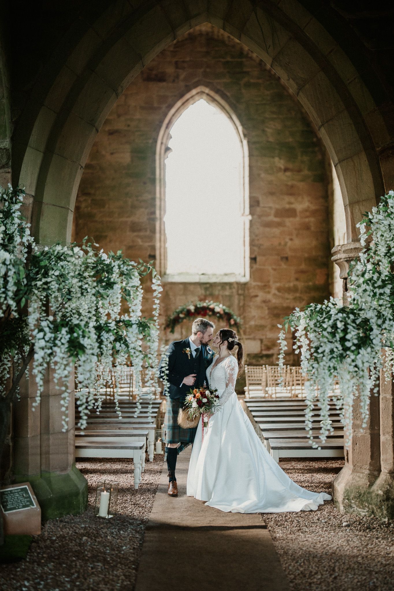 Wedding couple poses in a historic stone church archway decorated with elegant white floral arrangements.
