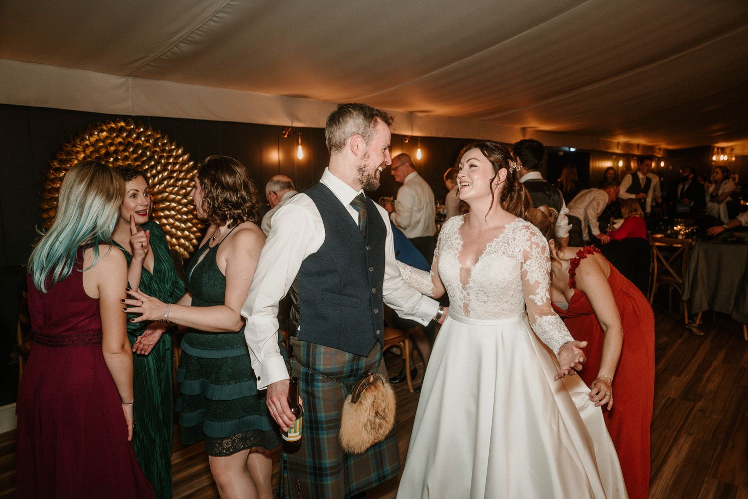 Wedding guests dancing and celebrating at a reception with warm lighting.