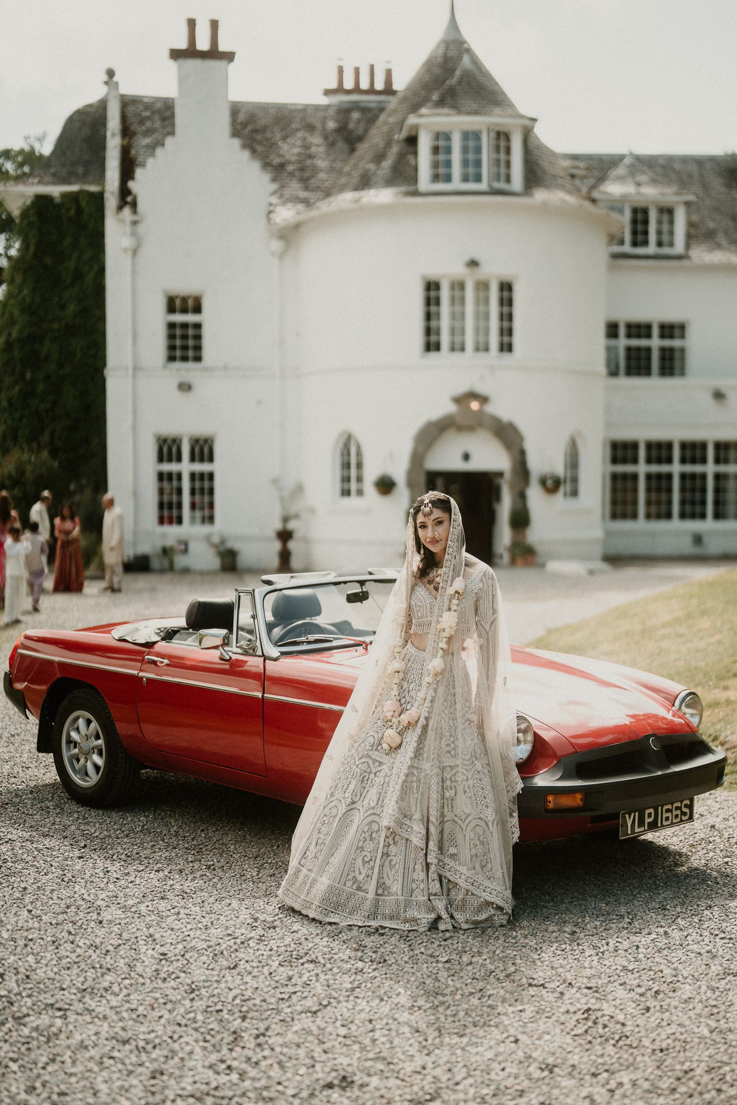 Classic red convertible sports car parked in front of elegant white mansion wedding venue.