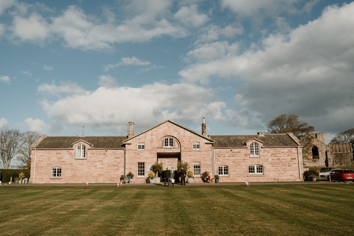 Large pink stone country house with symmetrical windows and arched entrance on sprawling lawn.