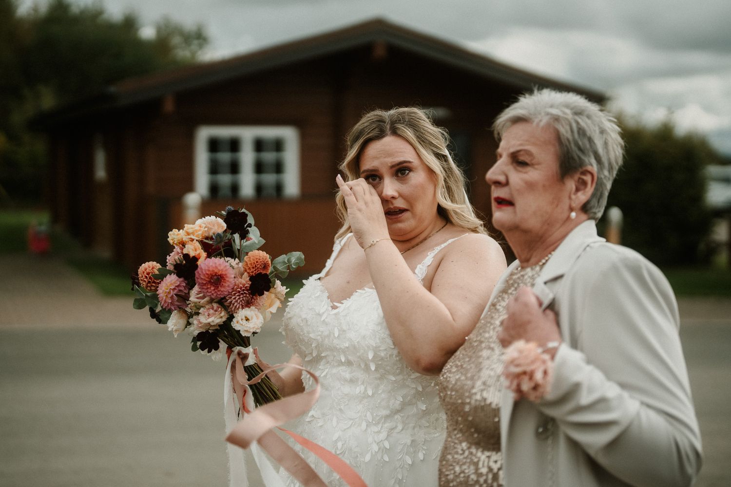 Wedding party in mix of white and earth tone dresses gathered outside rustic venue.