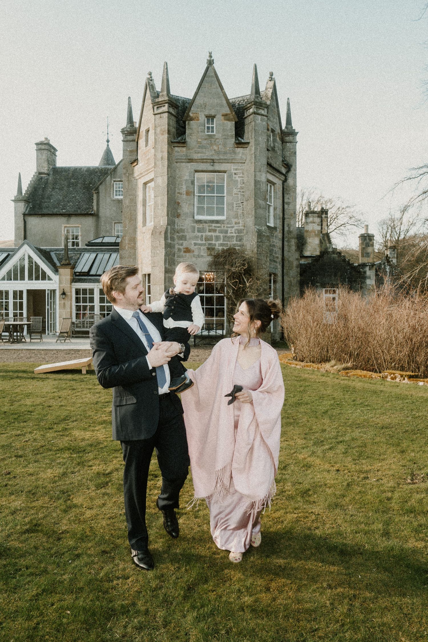 Elegant gathering outside a historic Scottish castle with conservatory in background.