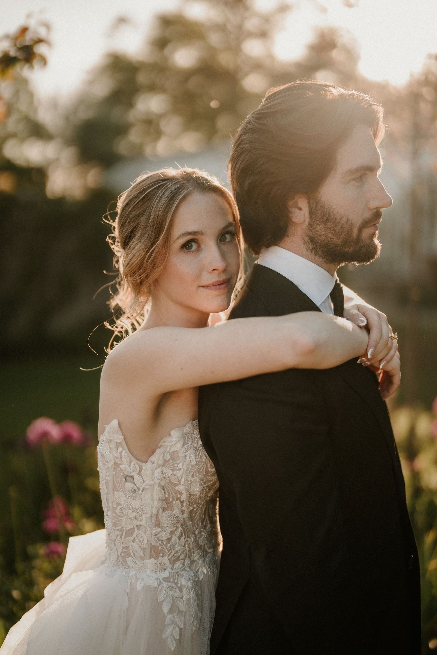Romantic wedding couple poses together during golden hour sunset in an outdoor garden setting.