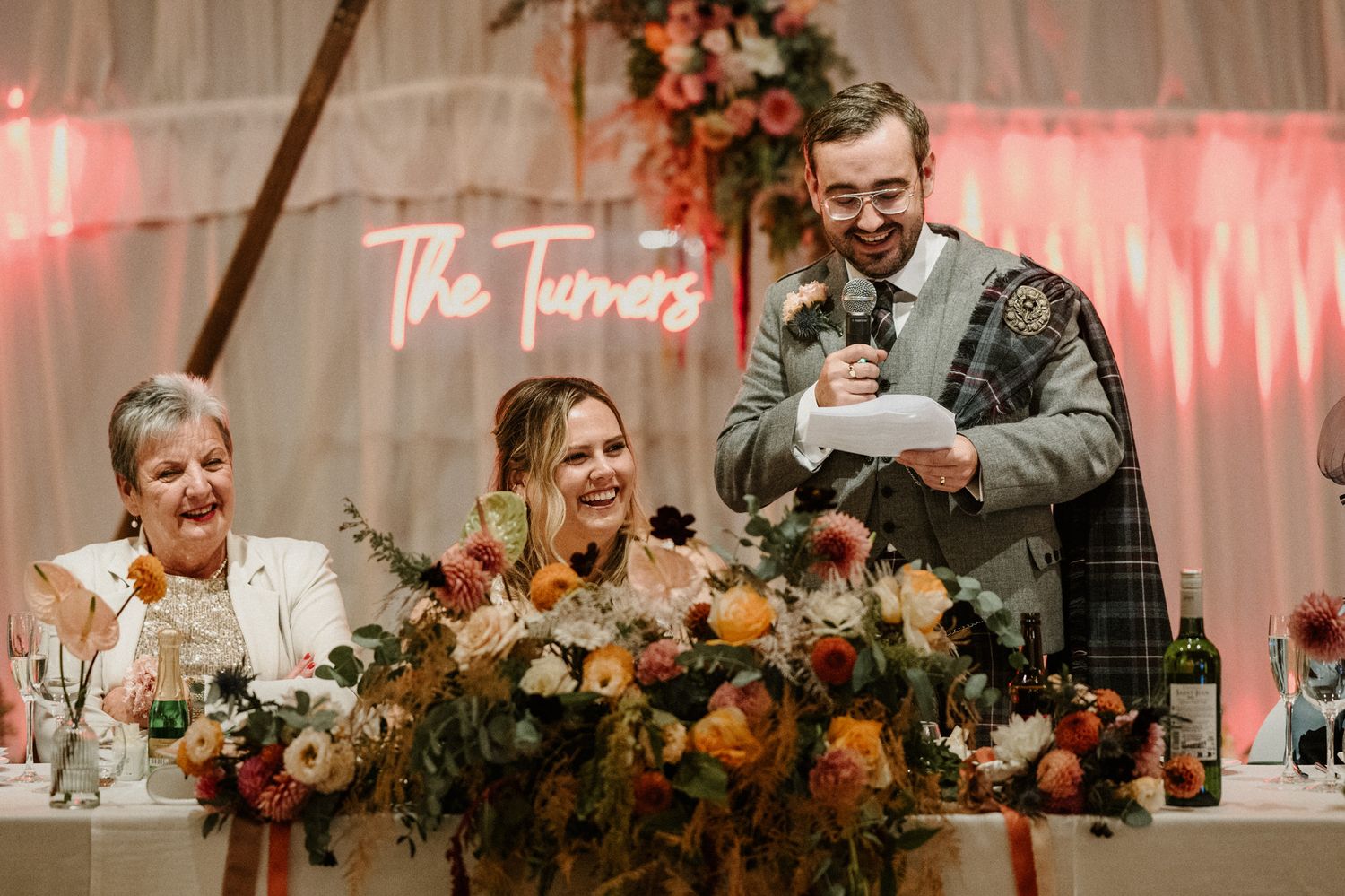 Scottish wedding reception with laughter during speeches at decorated head table.