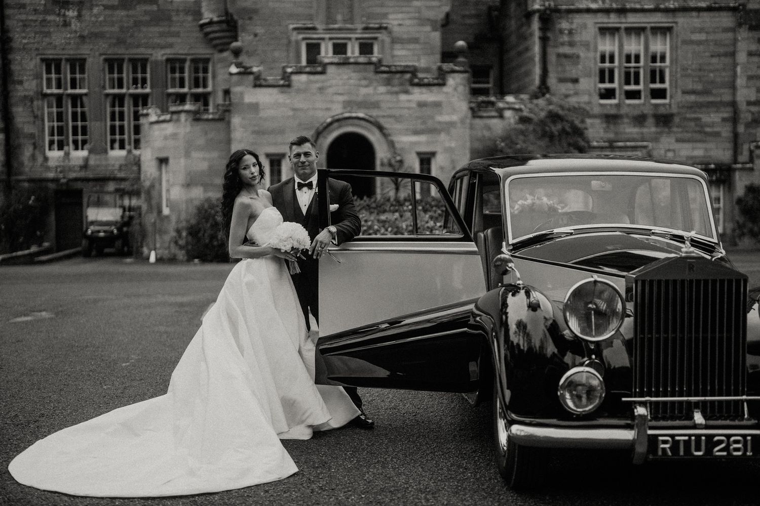 Classic vintage cars parked outside stone building during wedding celebration.