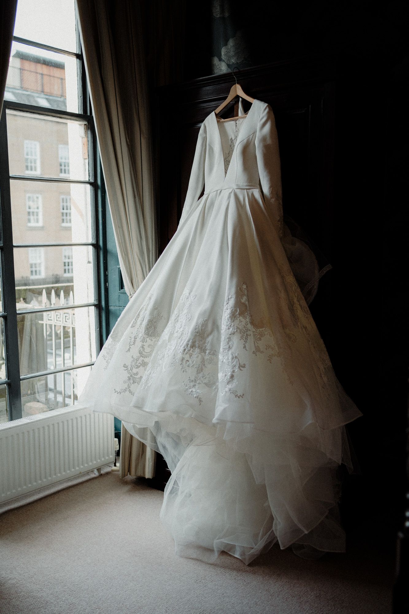Elegant white wedding dress hanging by window in natural light.