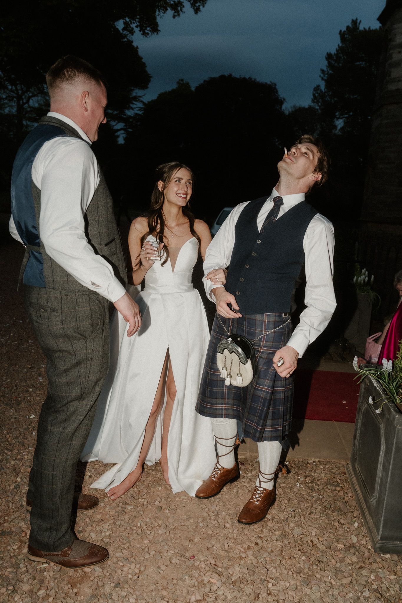 Bride in white gown with groom in kilt and tartan at outdoor evening wedding celebration.