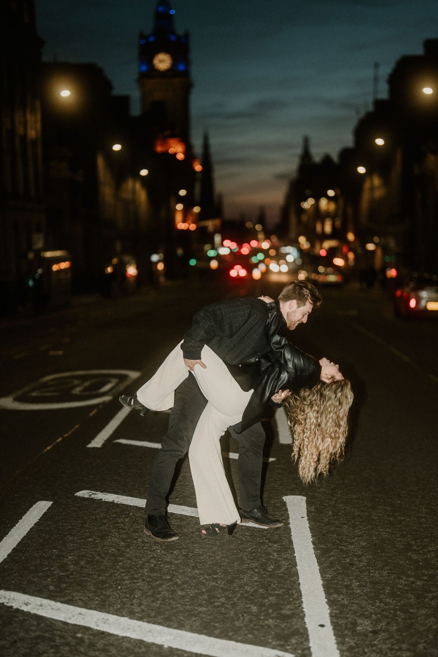 Couple sharing a romantic dip kiss on a city street at night with bokeh lights.