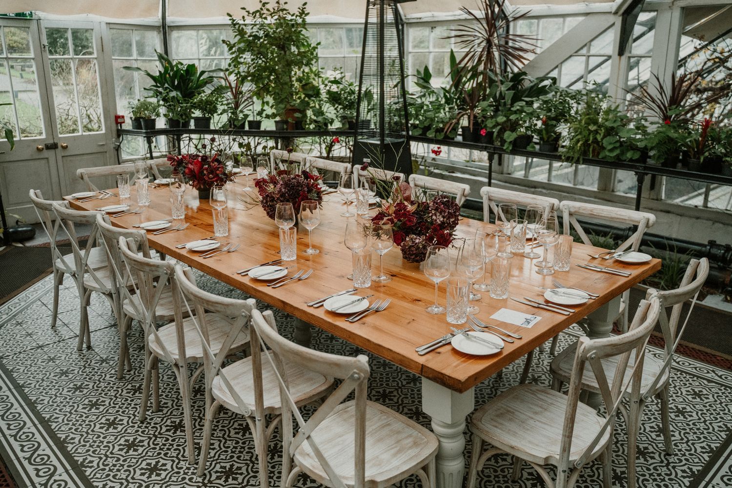 Elegant wedding reception tables set with white chairs and floral centerpieces in a bright conservatory setting.