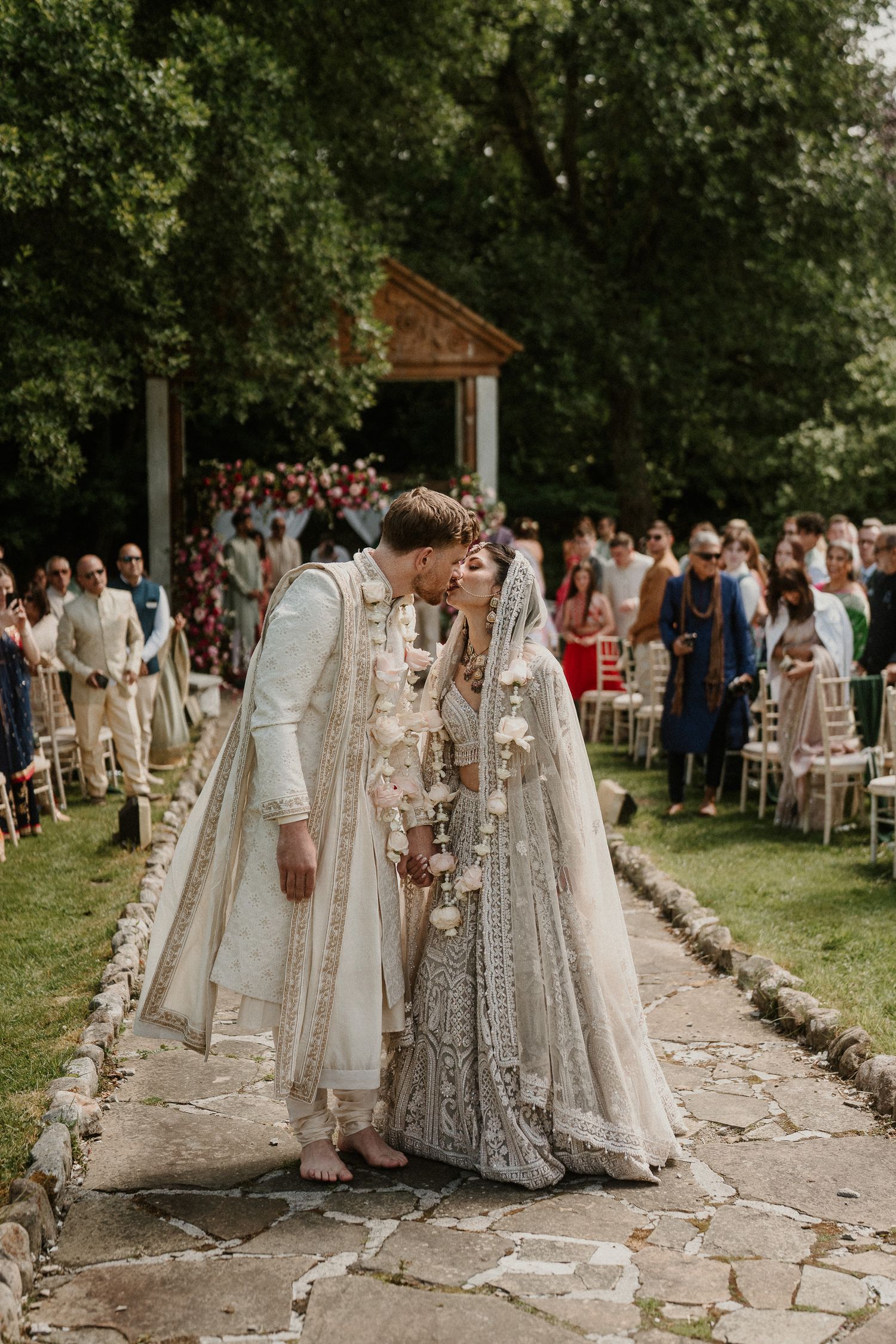 Outdoor wedding ceremony with guests seated in white chairs along a stone pathway.
