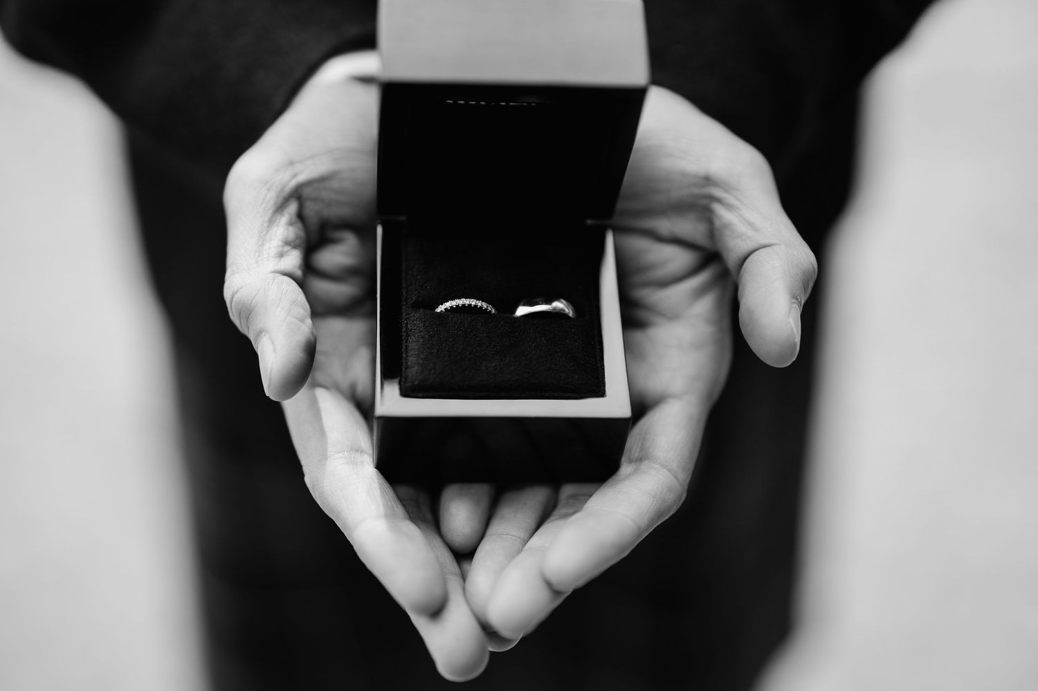Close-up of hands holding wedding rings in black jewelry boxes.