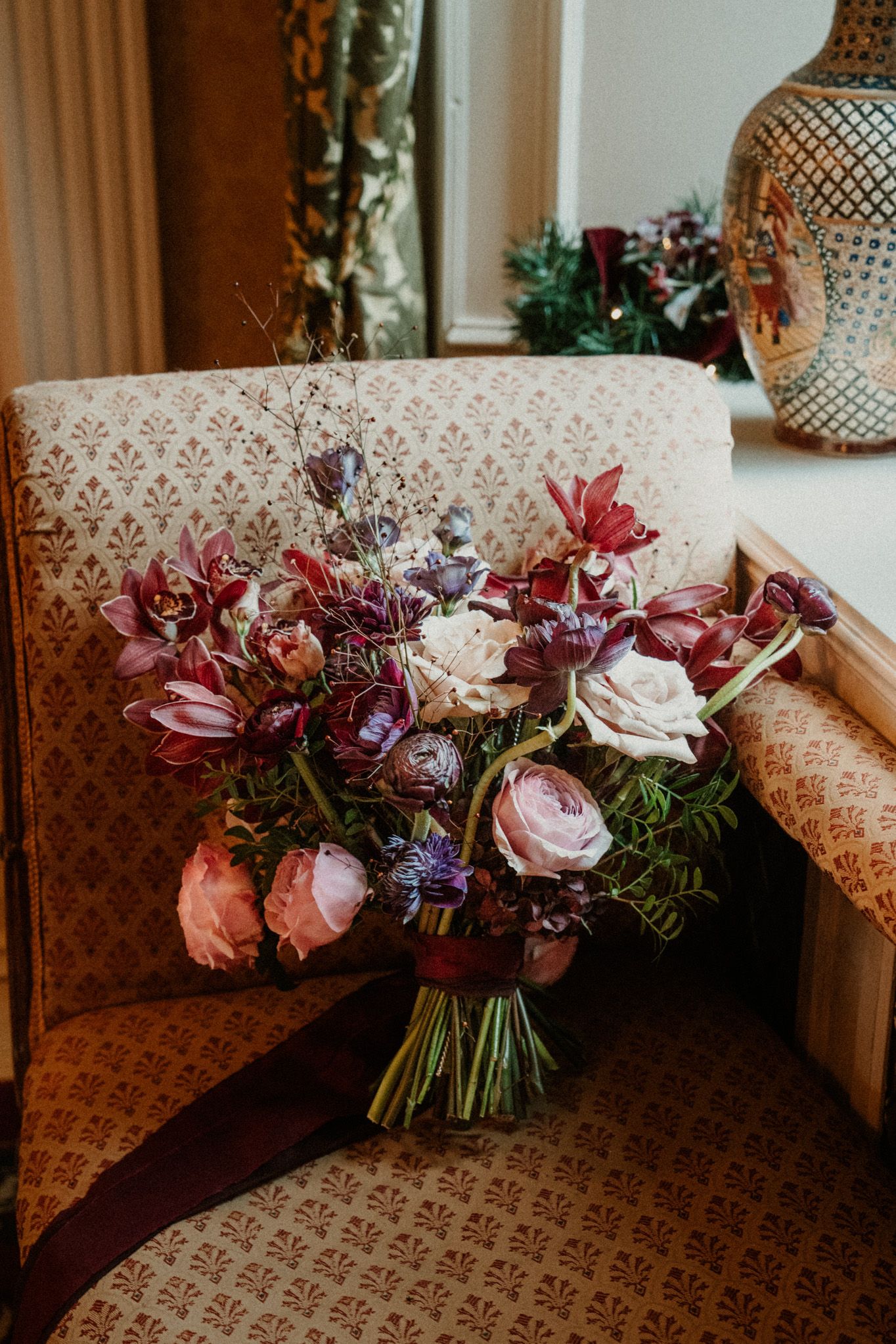 Beautiful wedding bouquet with pink roses and burgundy flowers displayed on a patterned sofa.