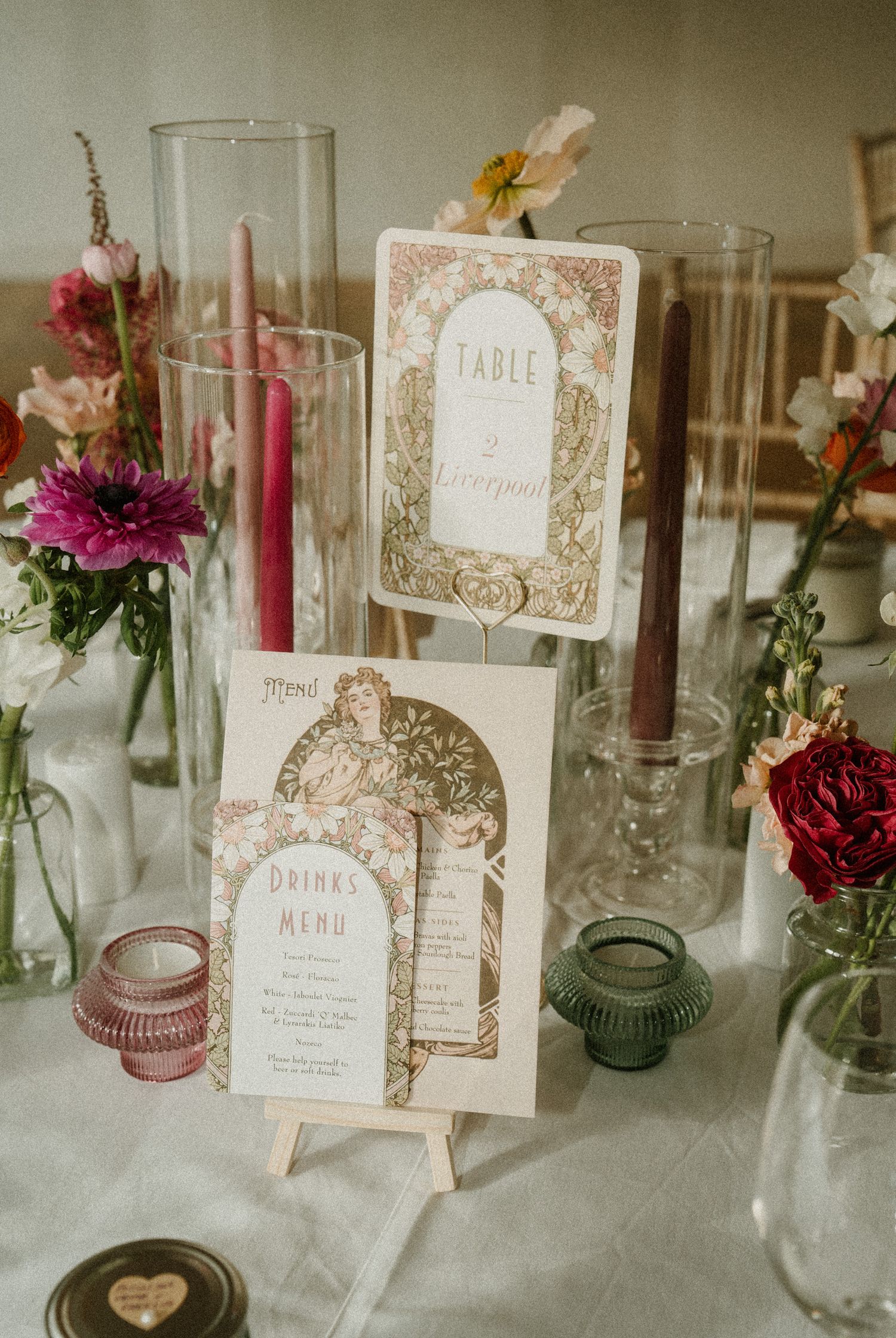 Vintage-style wedding table cards and menu with floral designs displayed among glass vases and candle holders.