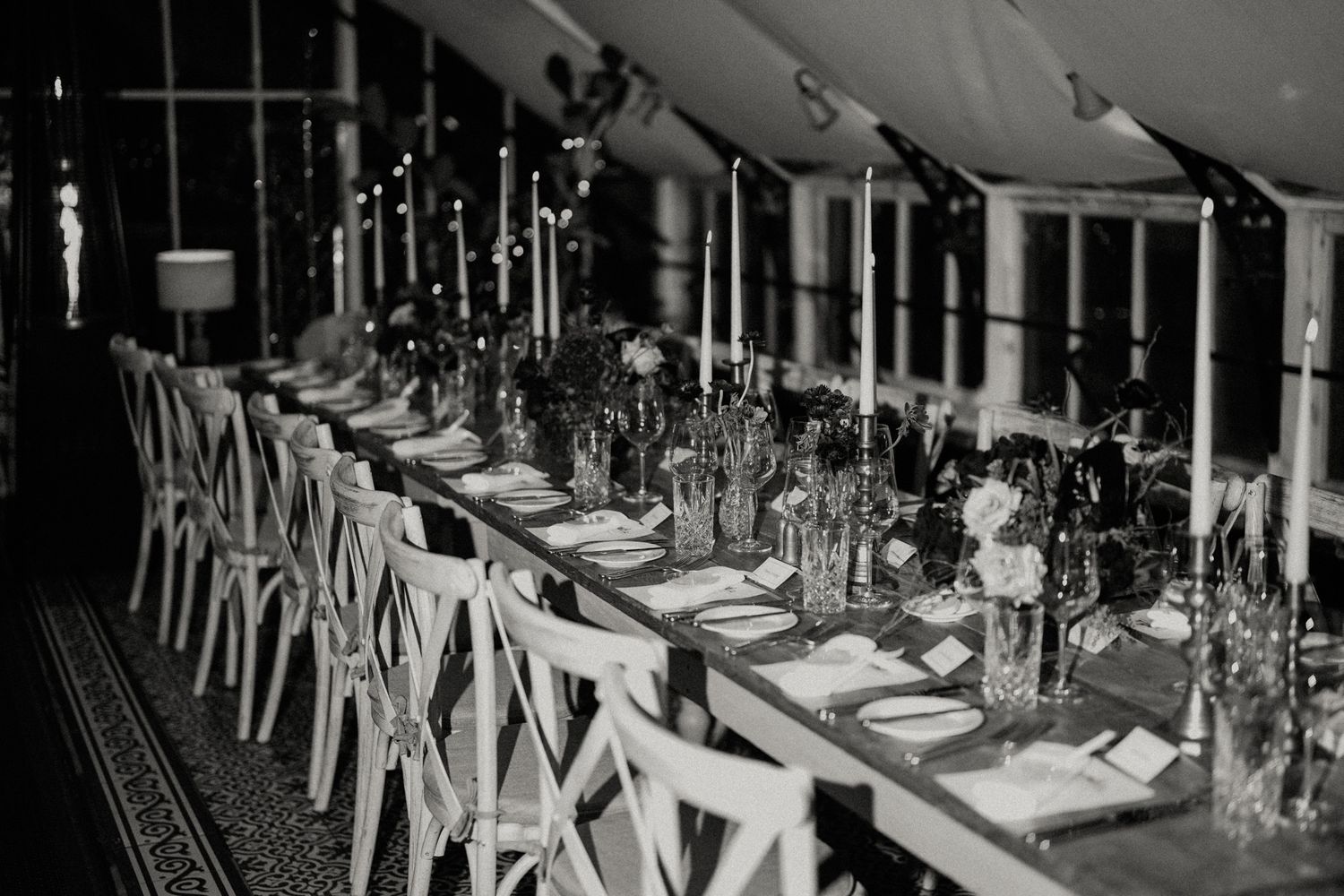 Elegant wedding reception table setting with white chairs and crystal glassware in black and white.