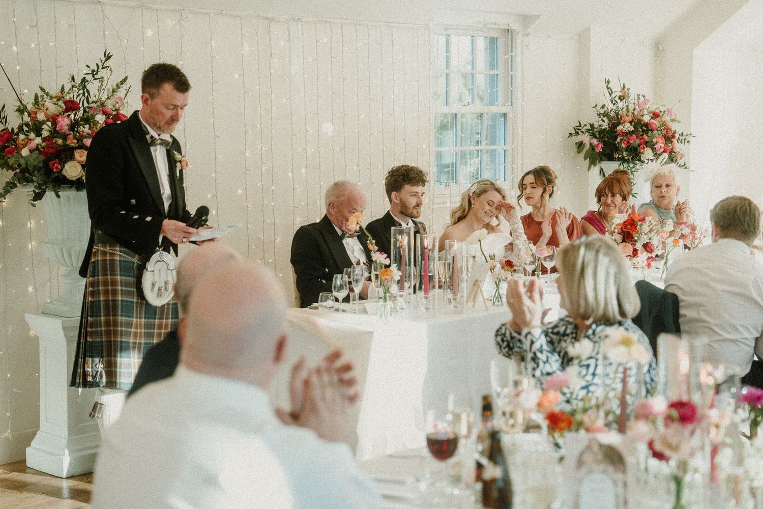 Wedding reception venue with elegant table settings and floral arrangements in a bright white room.