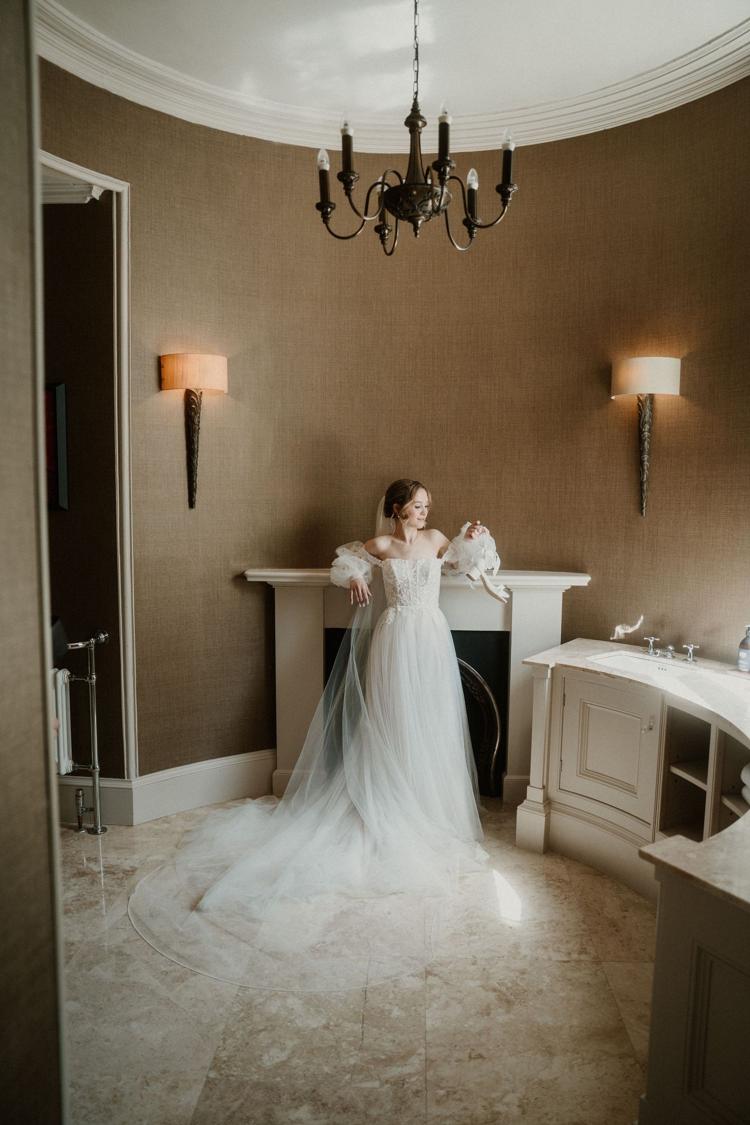 Wedding dress displayed in an elegant room with chandelier and neutral walls.