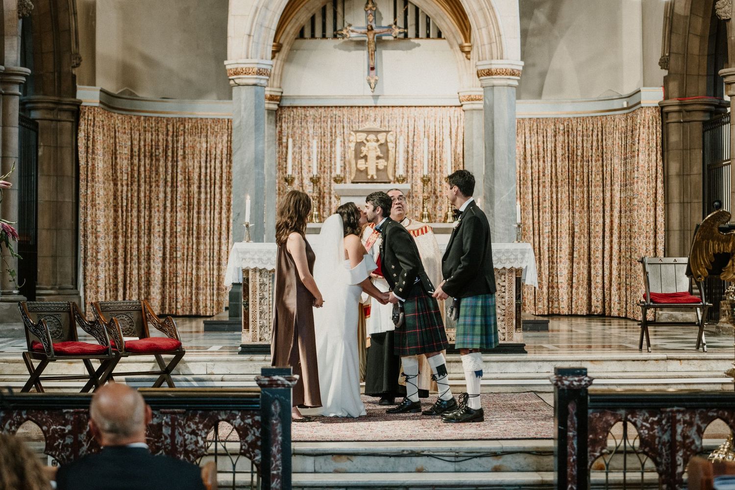 Intimate wedding ceremony at church altar with Scottish traditional elements and formal attire.