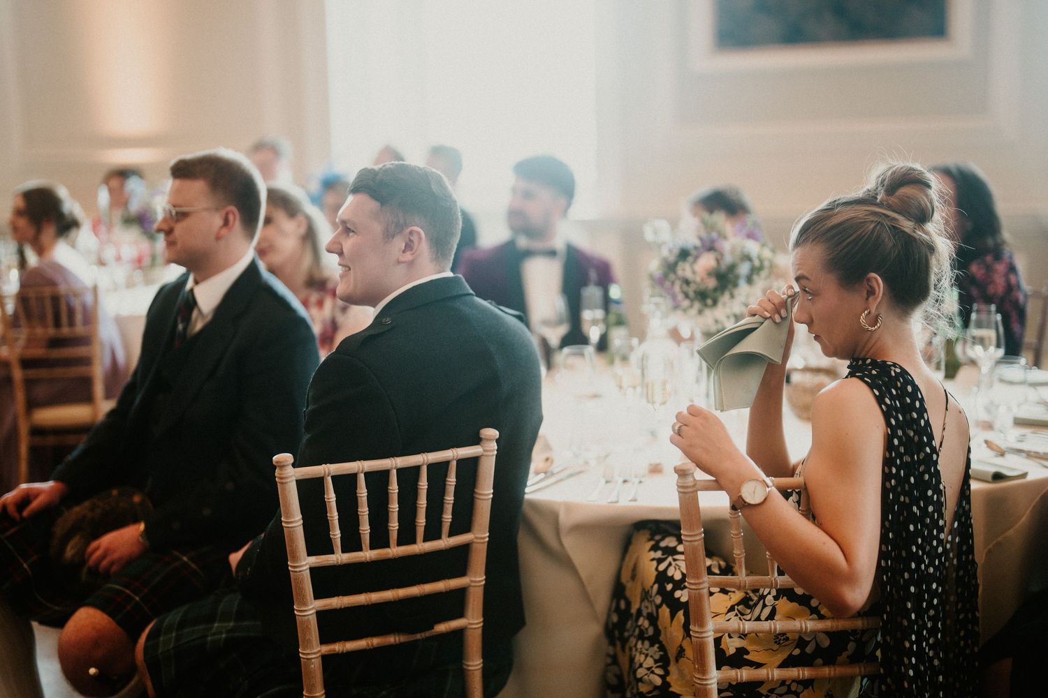 Wedding reception guests seated at formal dining tables in elegant ballroom setting.