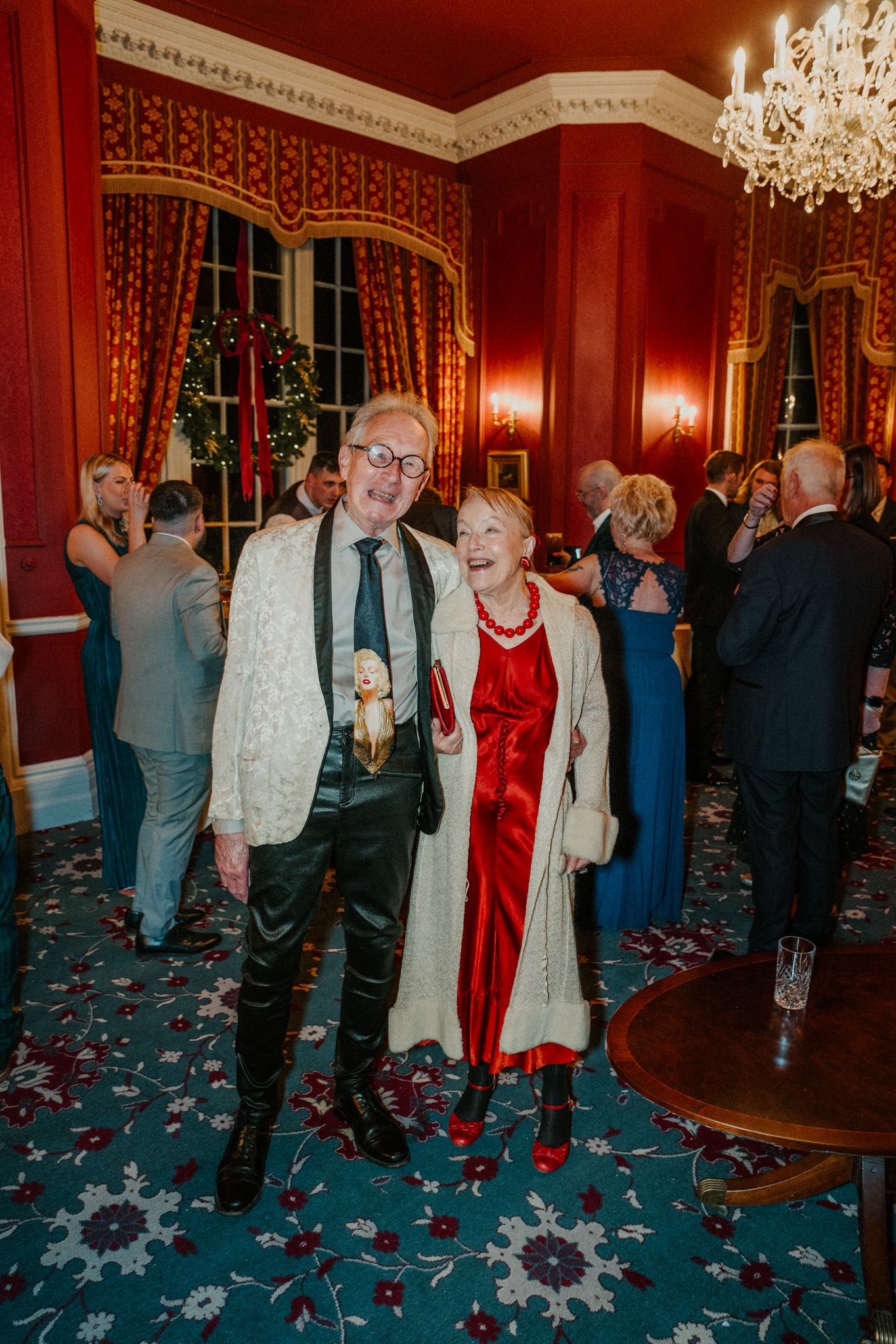 Wedding celebration in an elegant red room with crystal chandelier and ornate decor.