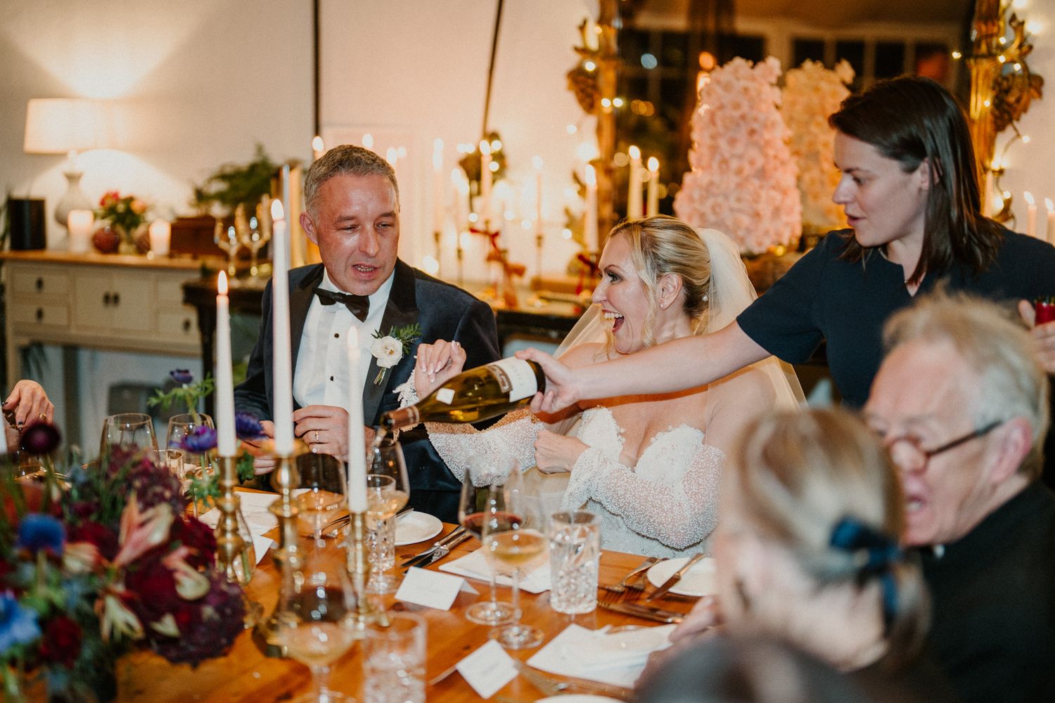 Intimate dinner party setting with guests seated at a long table under warm lighting.