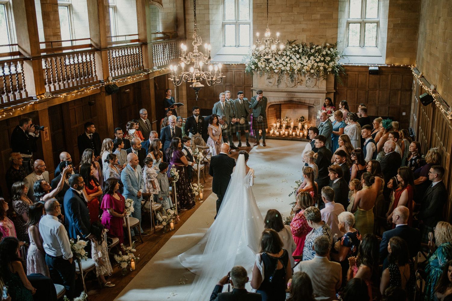Church wedding ceremony with guests standing in wooden pews under vaulted ceilings.