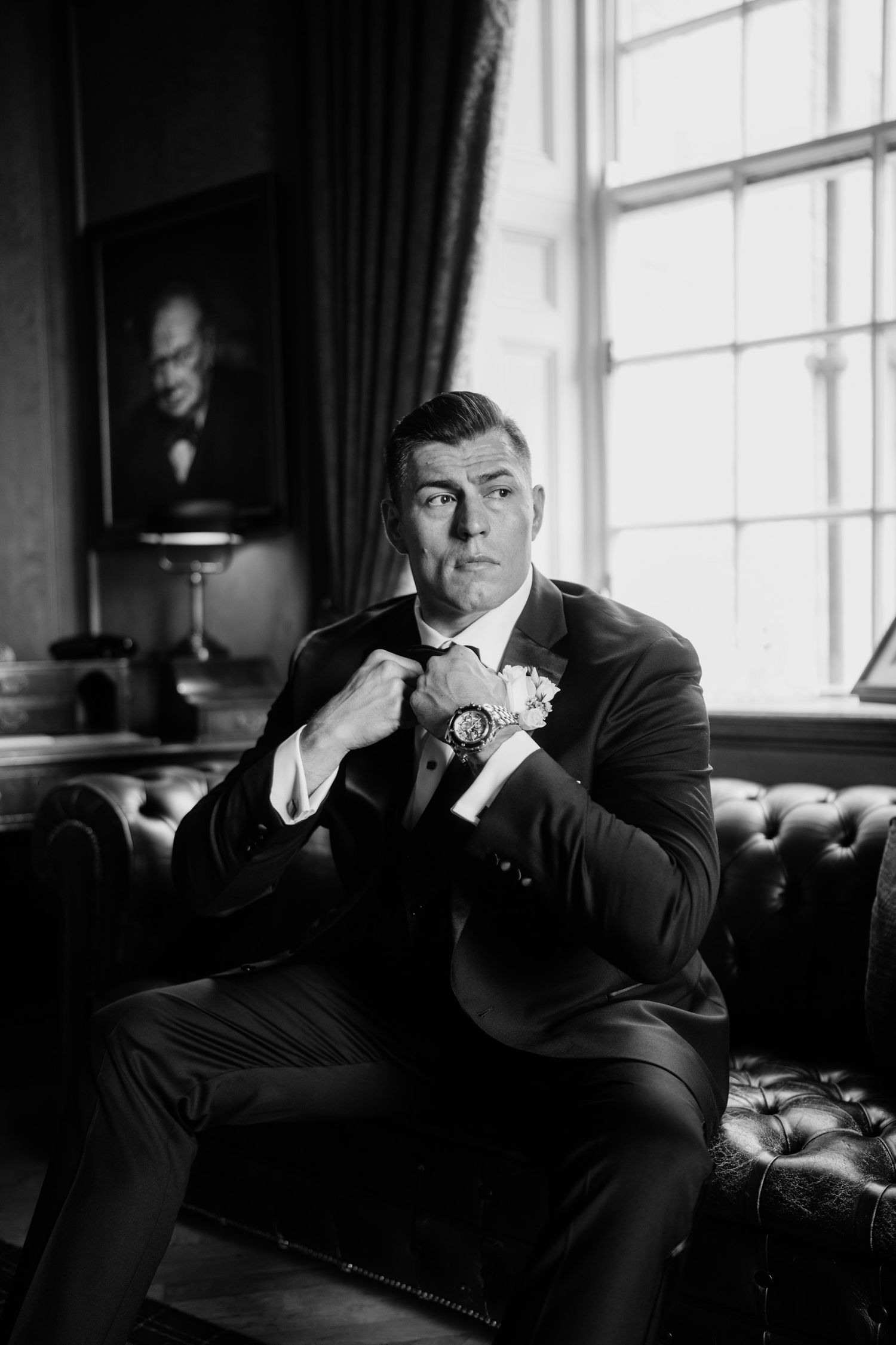 Black and white portrait of someone in formal attire lounging on leather furniture.