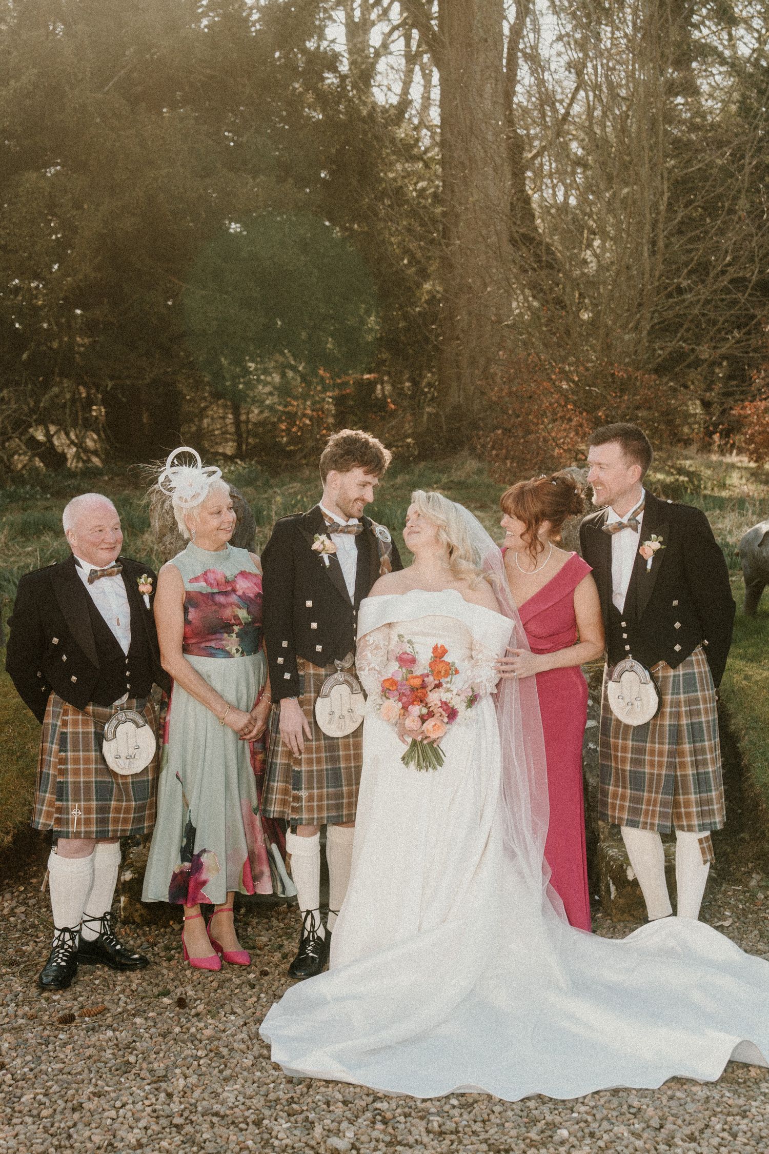 Wedding group arranges for photos on a gravel path surrounded by autumn trees.