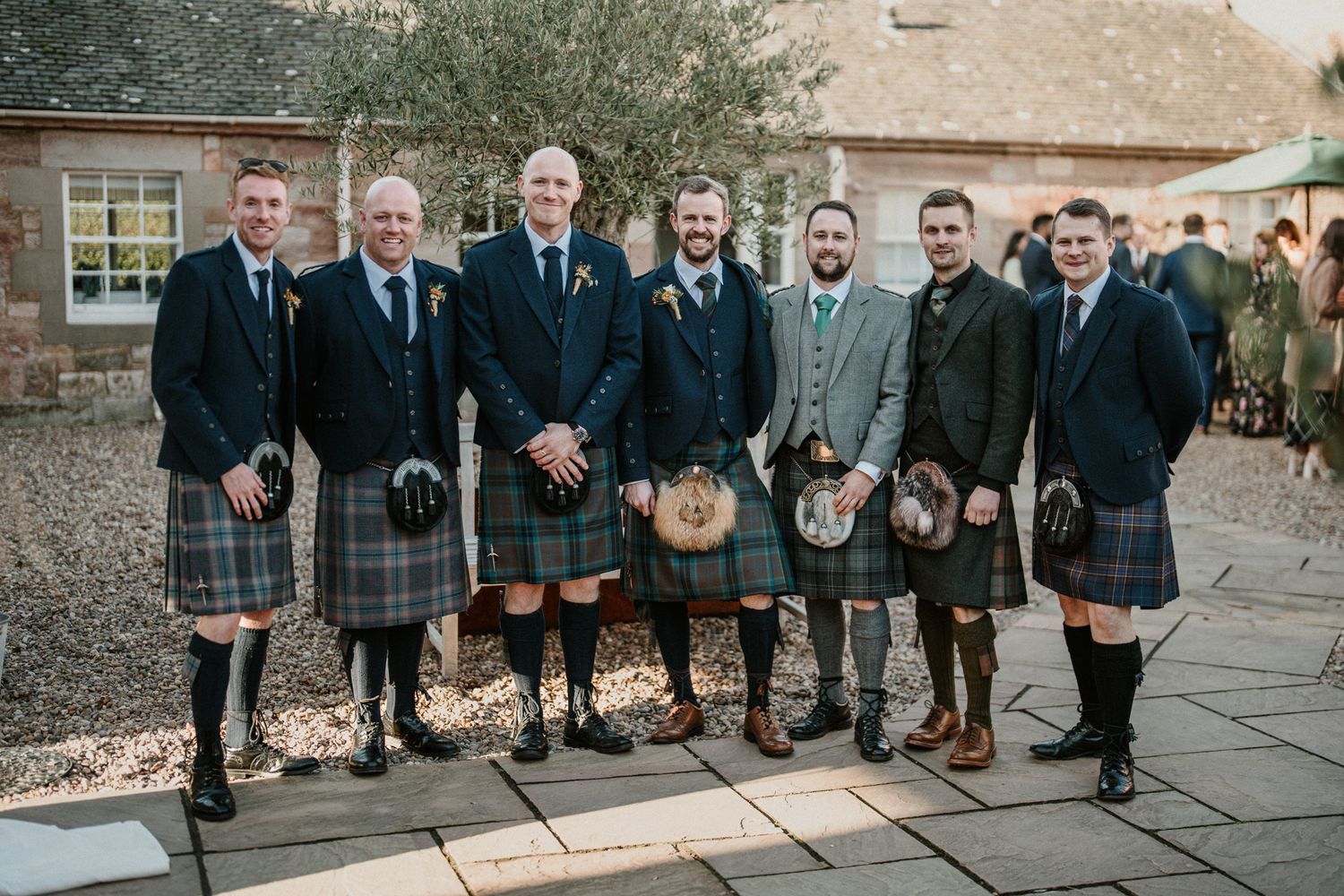 Wedding party members in traditional Scottish kilts and formal attire lined up for a photo.