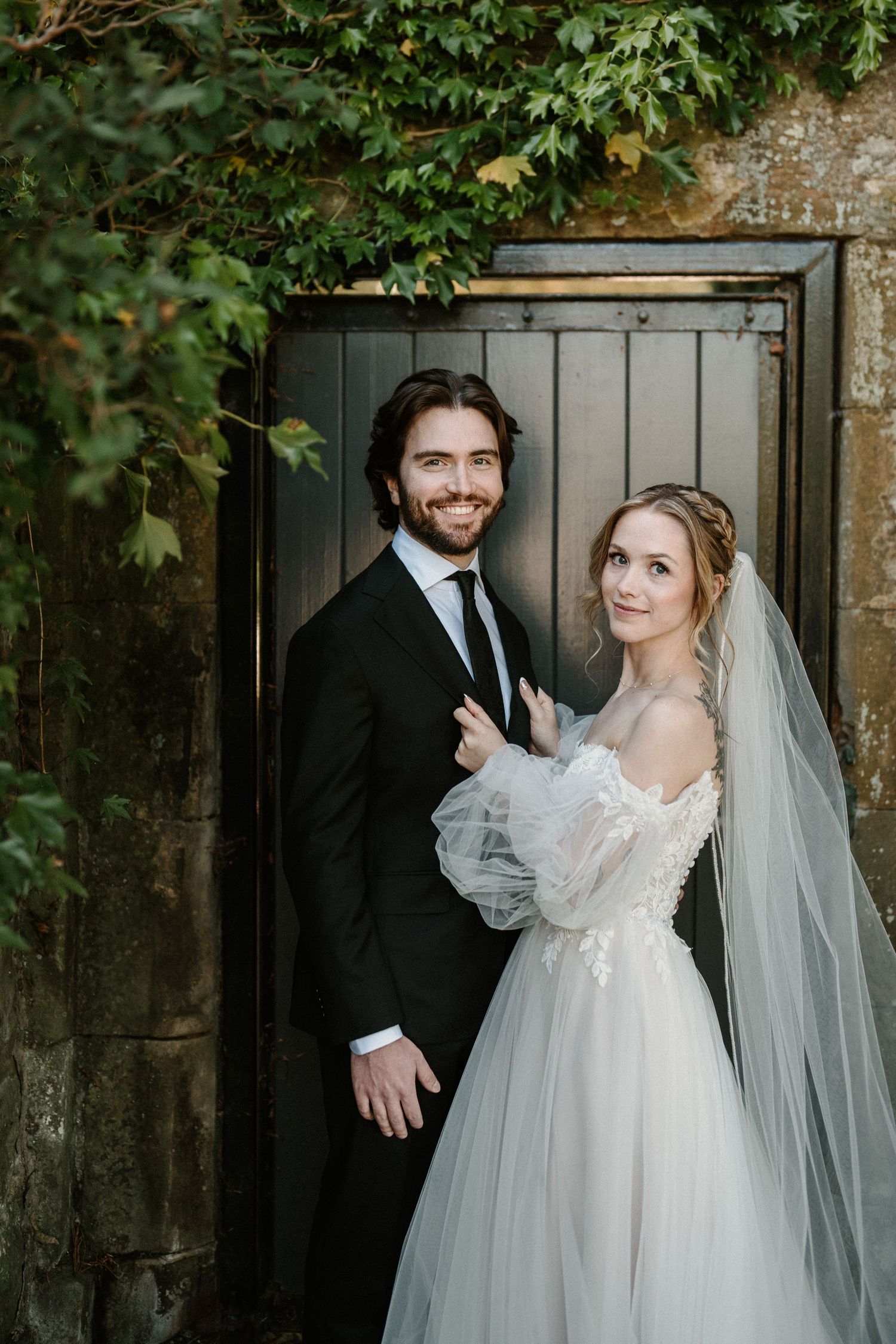 Romantic wedding portrait by black gate with ivy and stone wall backdrop.