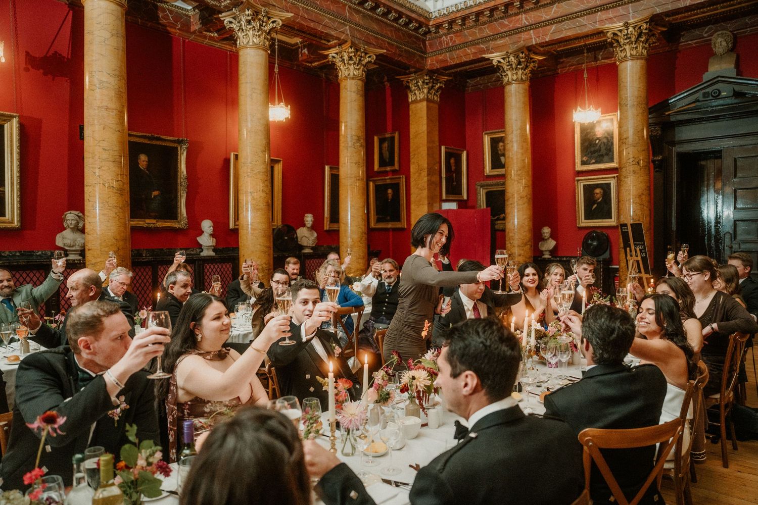 Panoramic view of a luxurious red ballroom with classical columns and crystal chandeliers.