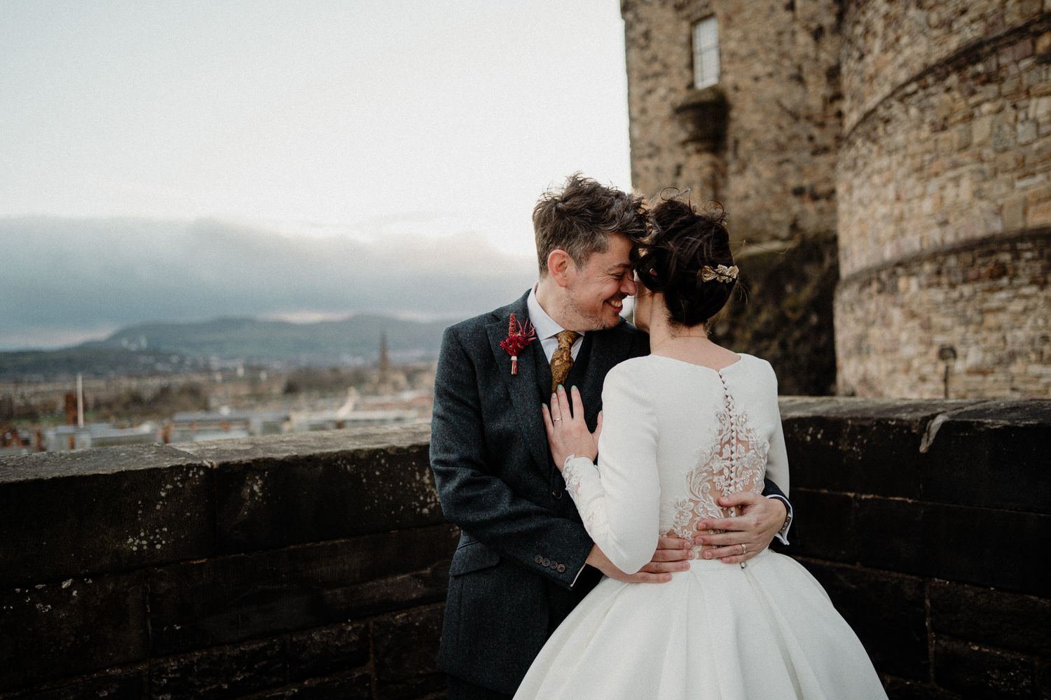 Newlyweds share an intimate moment against a historic castle backdrop with mountain views.