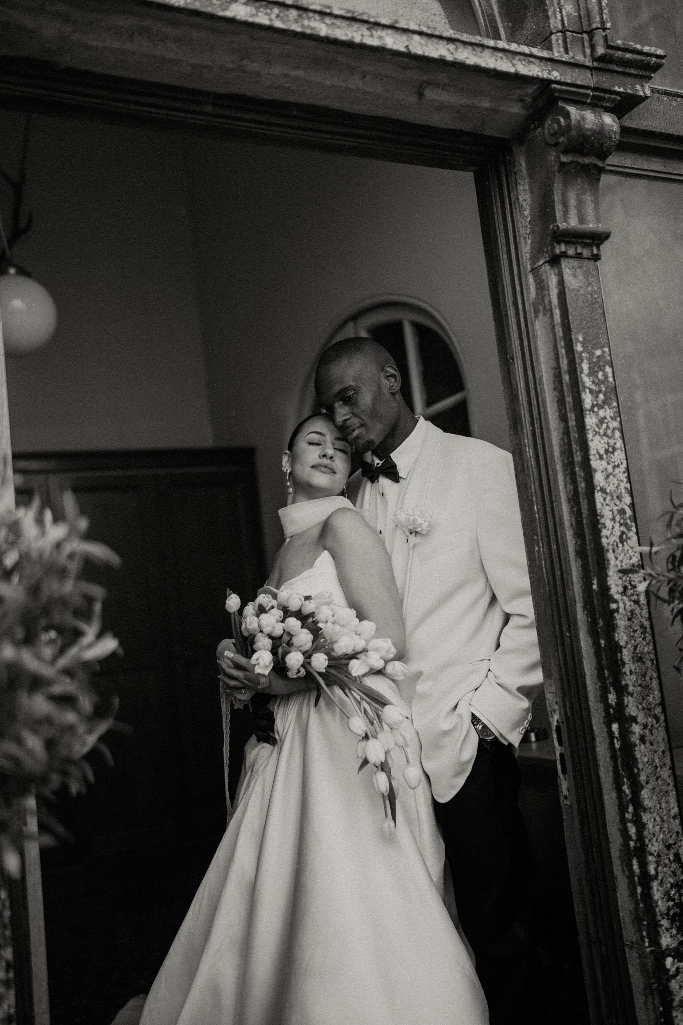 Black and white wedding photo series showing couple in elegant attire standing in doorway with flowers.