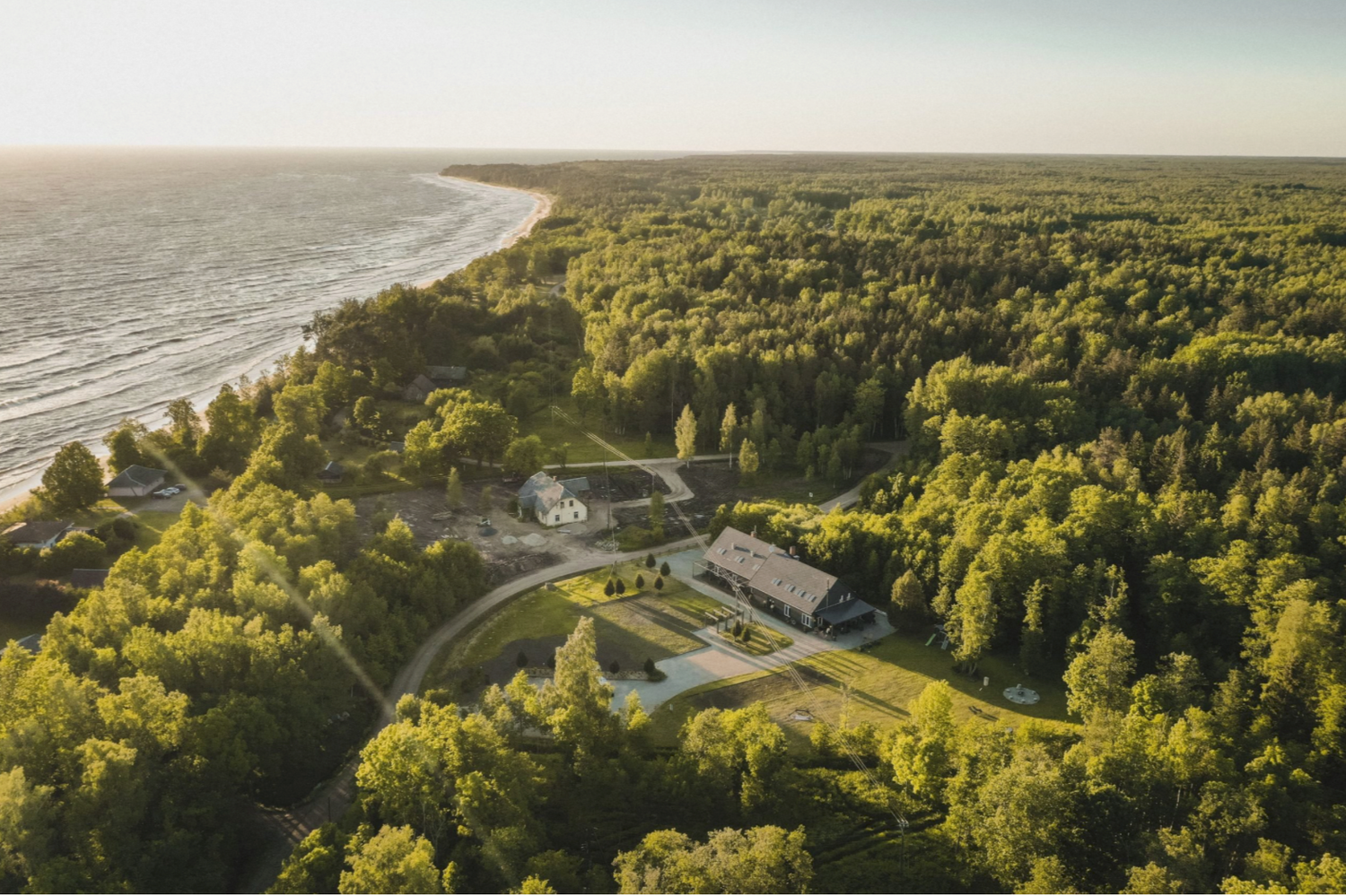 Aerial view of a secluded lodge surrounded by lush green forest along a scenic shoreline on a sunny day.
