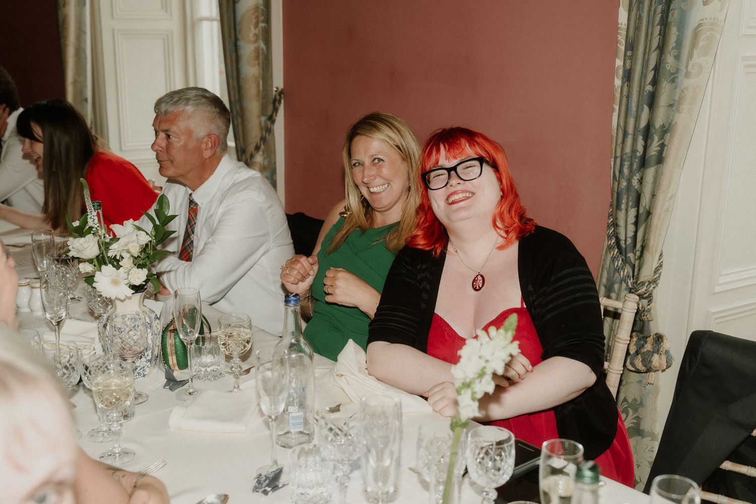 Wedding guests smile and celebrate at reception dinner table in elegant venue.