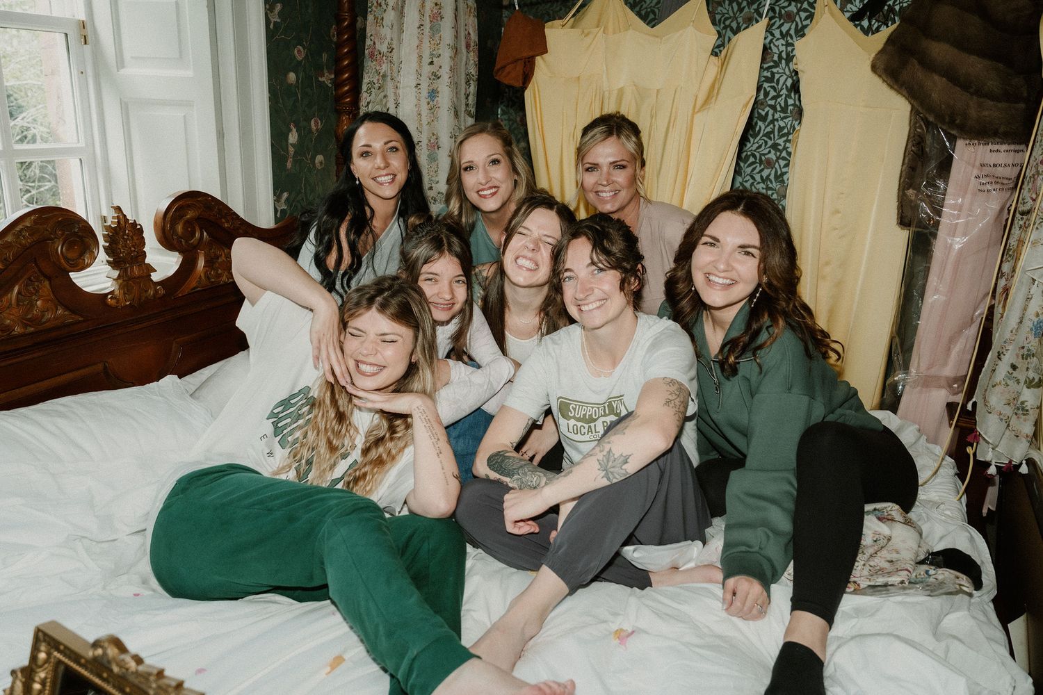 Group of women smiling and posing together on a bed in a decorated bedroom during a fun gathering.