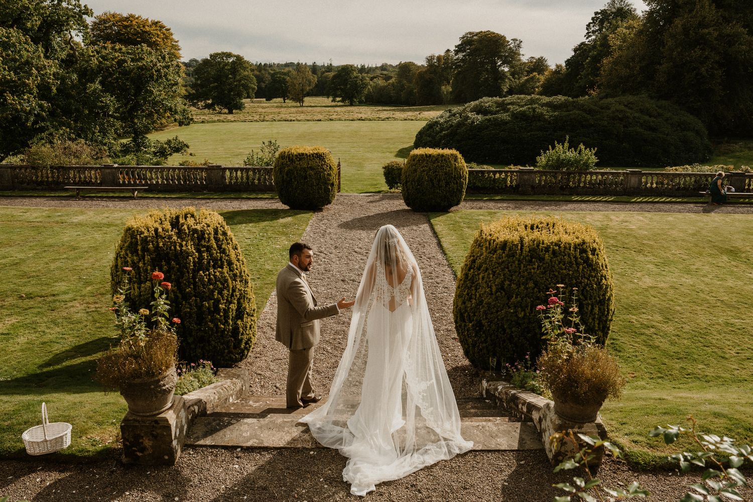 Bride and groom share a romantic moment in elegant formal garden with manicured hedges and sweeping lawn.