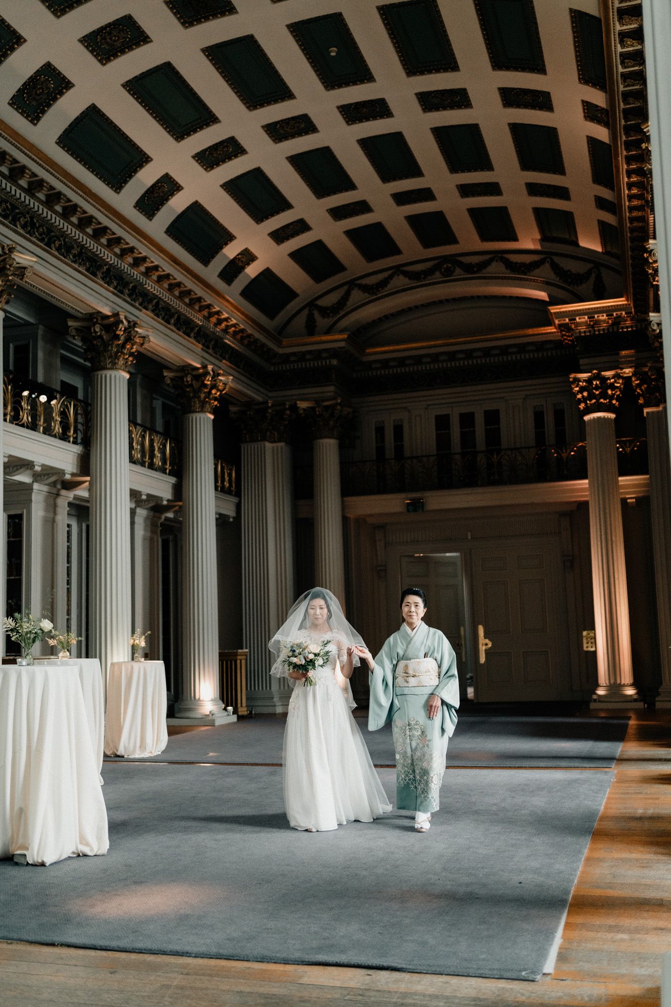 Grand ballroom with ornate coffered ceiling and classical columns set up for wedding ceremony.