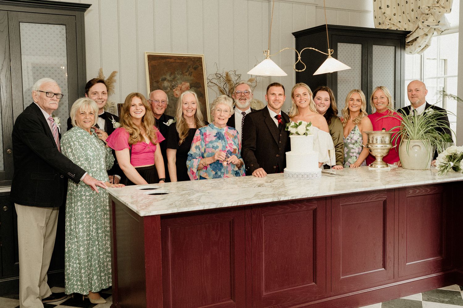 Wedding guests line up along a dark wood bar in formal attire.