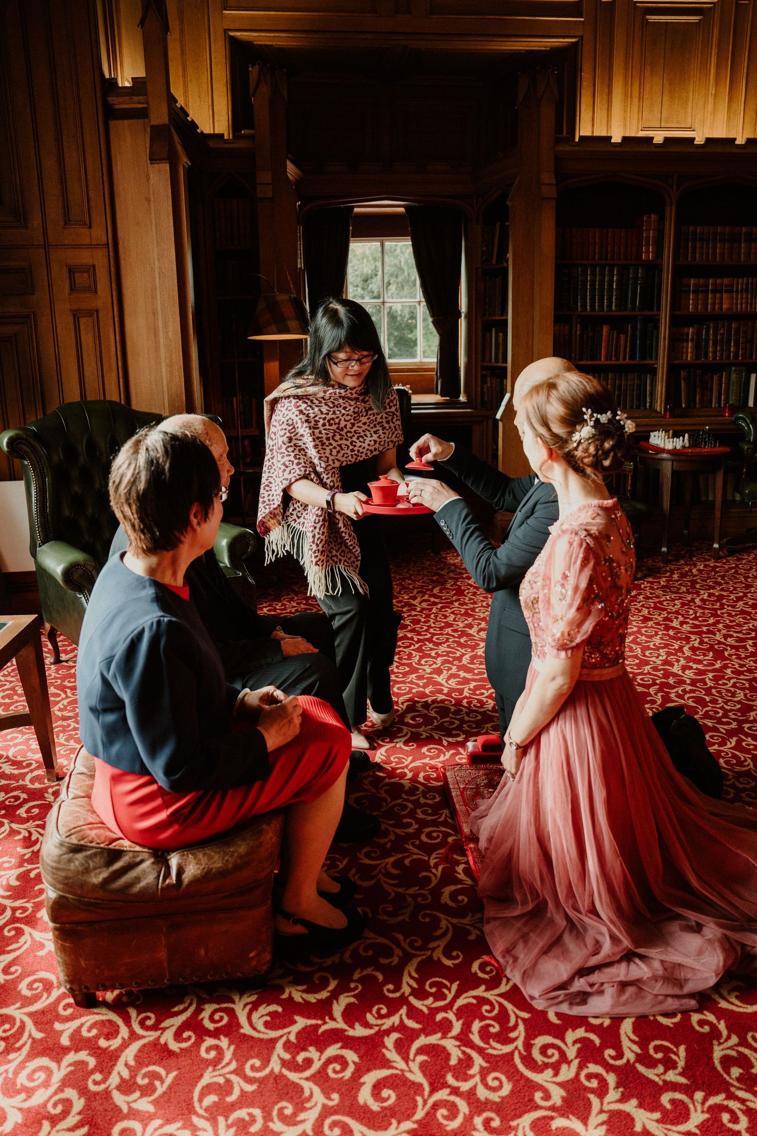 Group gathered in a library with wood paneling and red carpet discussing.