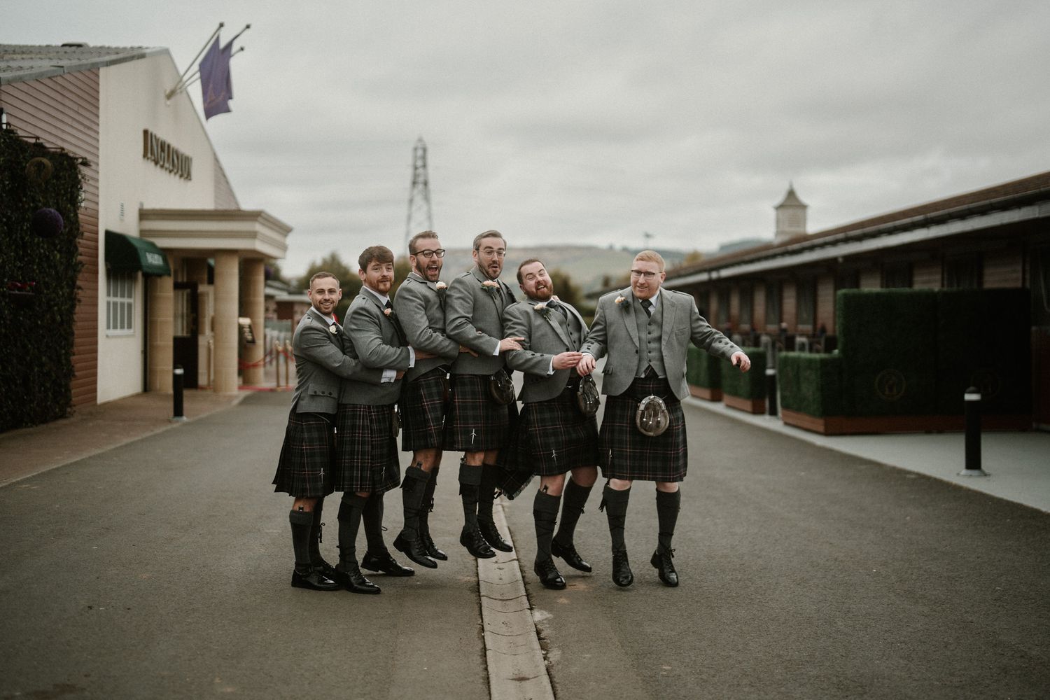 Wedding party in formal attire poses together outdoors on cloudy day.