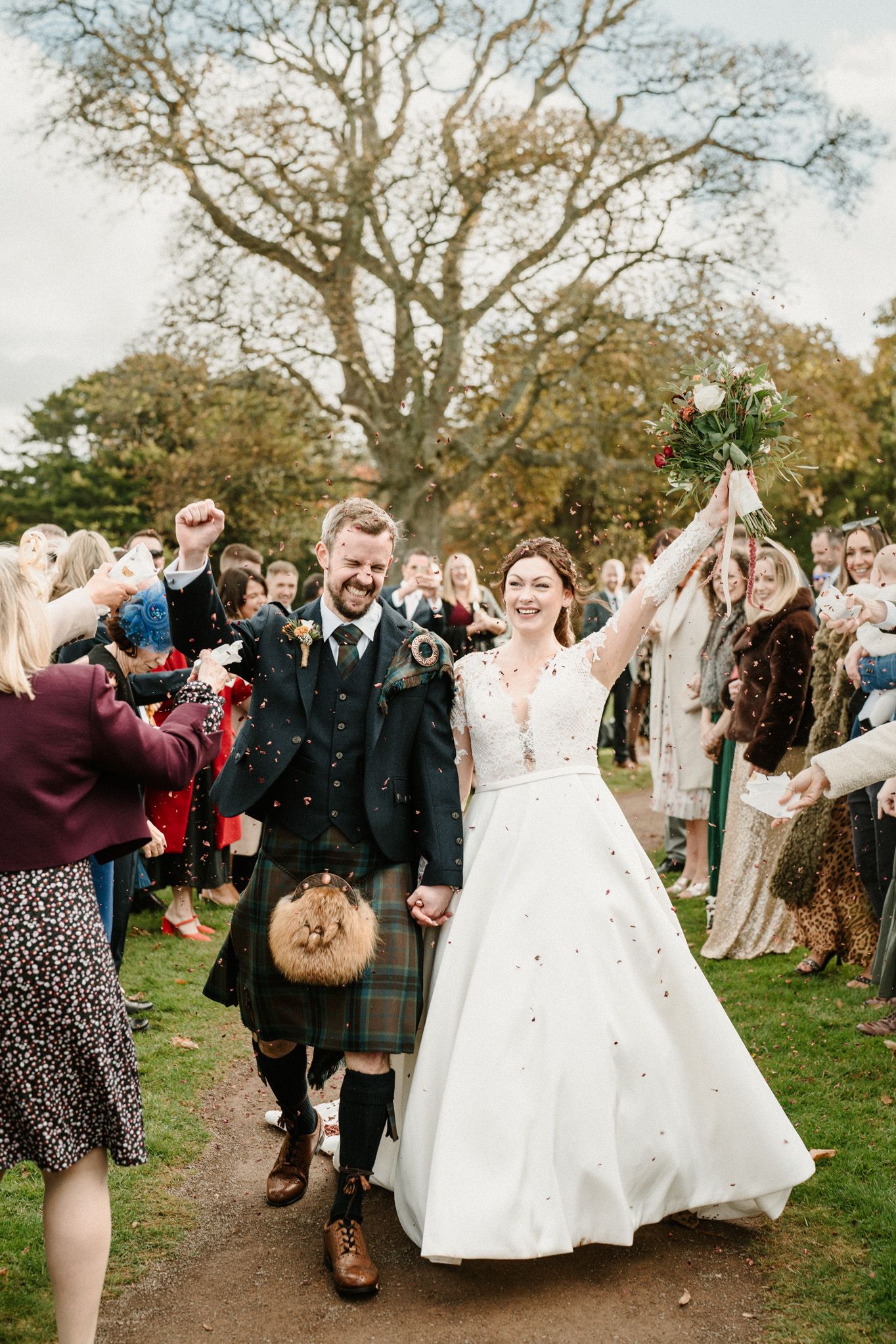 Wedding party walks through autumn grounds as guests throw confetti in celebration.