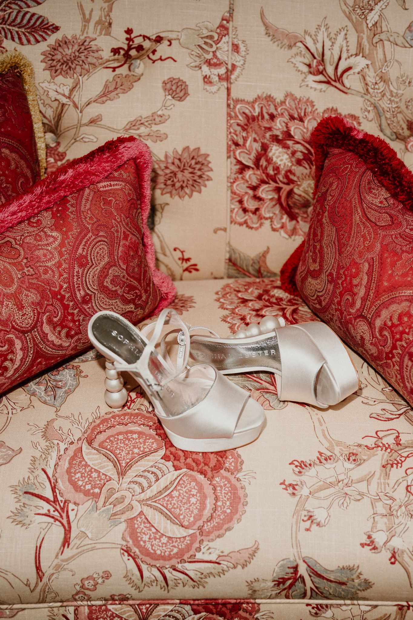 White bridal shoes placed on red and white toile patterned fabric.